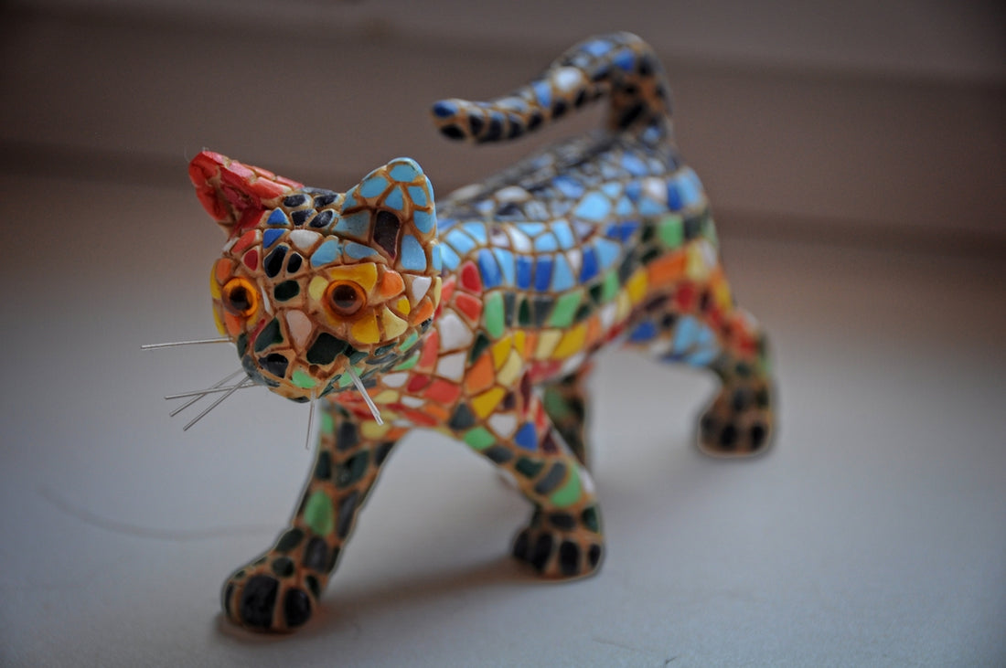 Mosaic cat statue walks on a window sill.